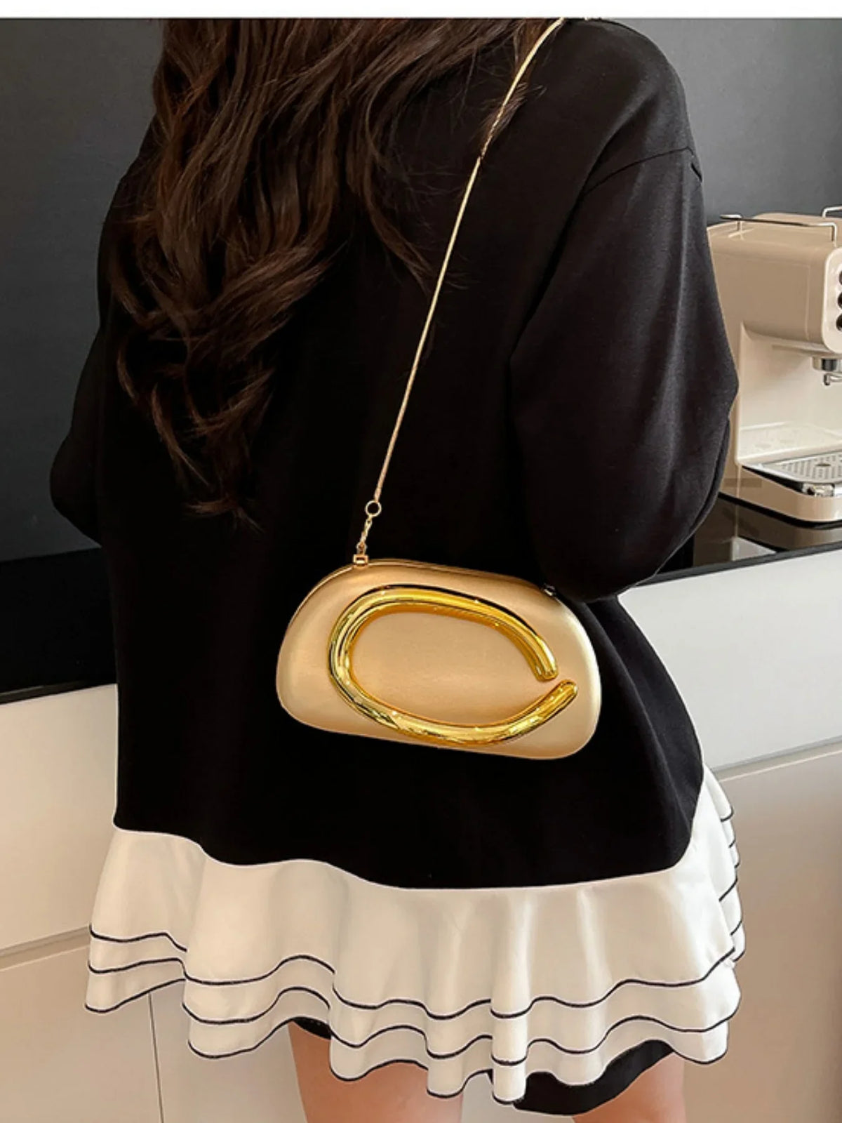 Elegant gold-accented handbag in a shell shape, worn on a shoulder, paired with a black top and white ruffled skirt.