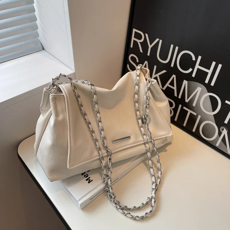 Soft beige shoulder bag with a silver chain strap, featuring a flap pocket and casual tote design.