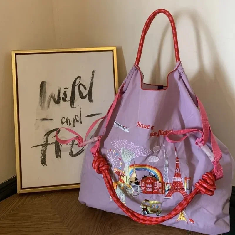 Large lilac nylon tote bag with embroidered travel-themed designs and red braided handles, ideal for casual use.