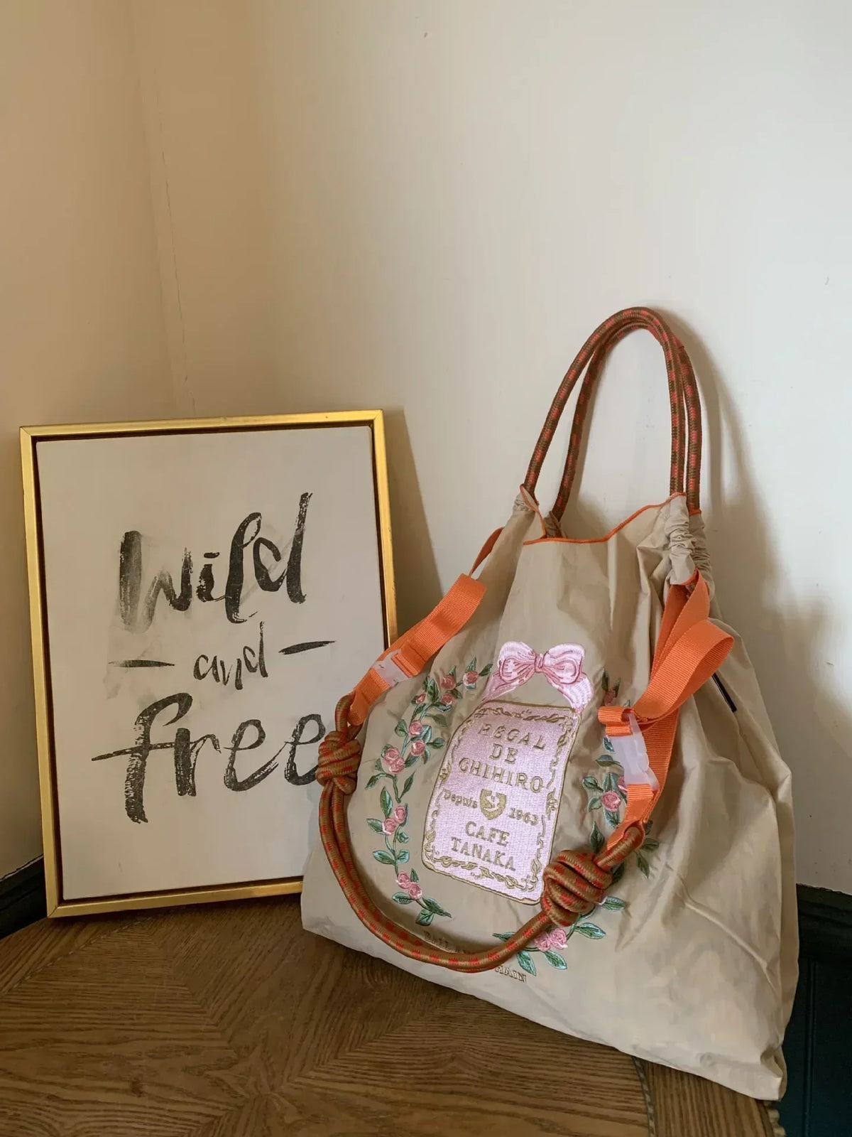 Large beige nylon tote bag with floral embroidery and vibrant orange straps, styled for casual use.