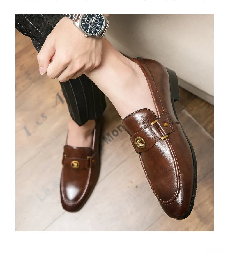 Slip-on brown leather loafers featuring a round toe and gold metal buckle detail, styled with pinstripe trousers.