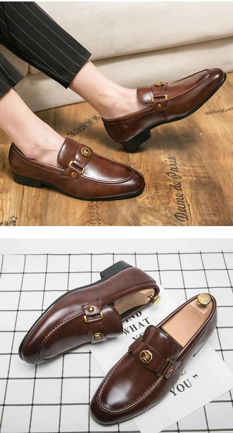 Brown leather slip-on loafers featuring a round toe and metal buckle detail, shown worn with pinstriped pants.