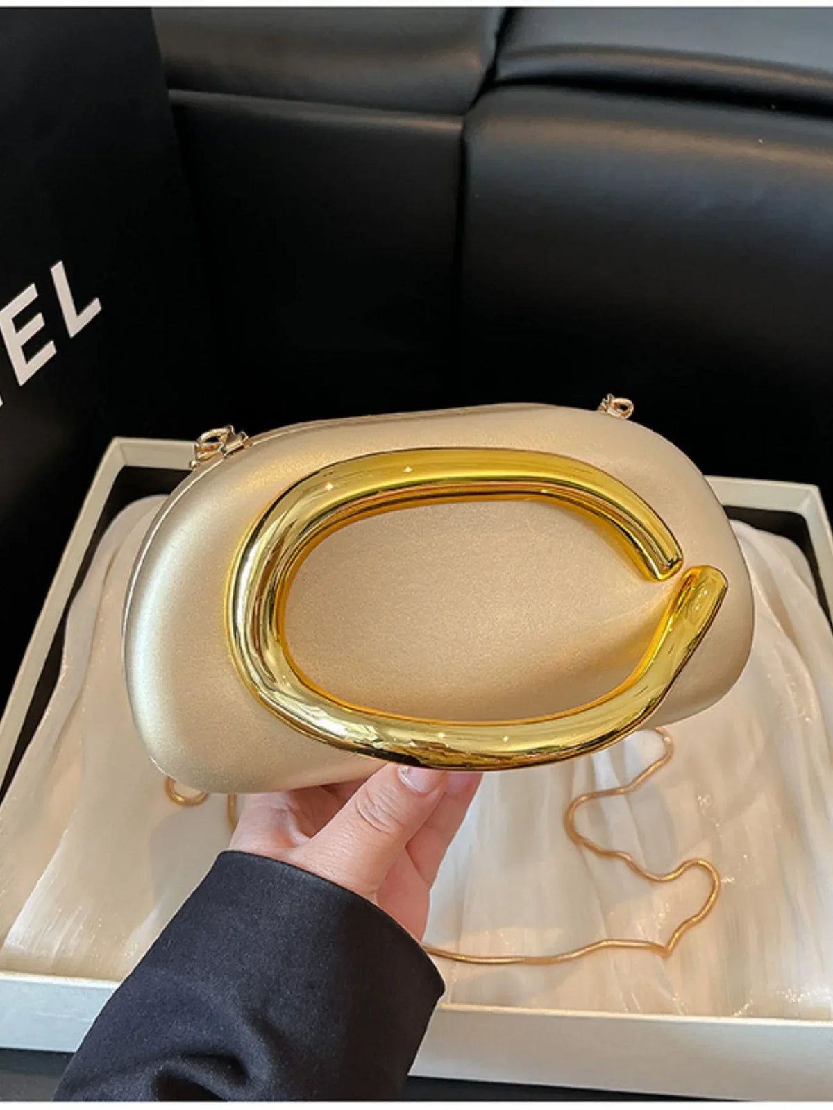 Elegant gold handbag with a shell-shaped design and a prominent gold handle, held in a hand against a dark background.