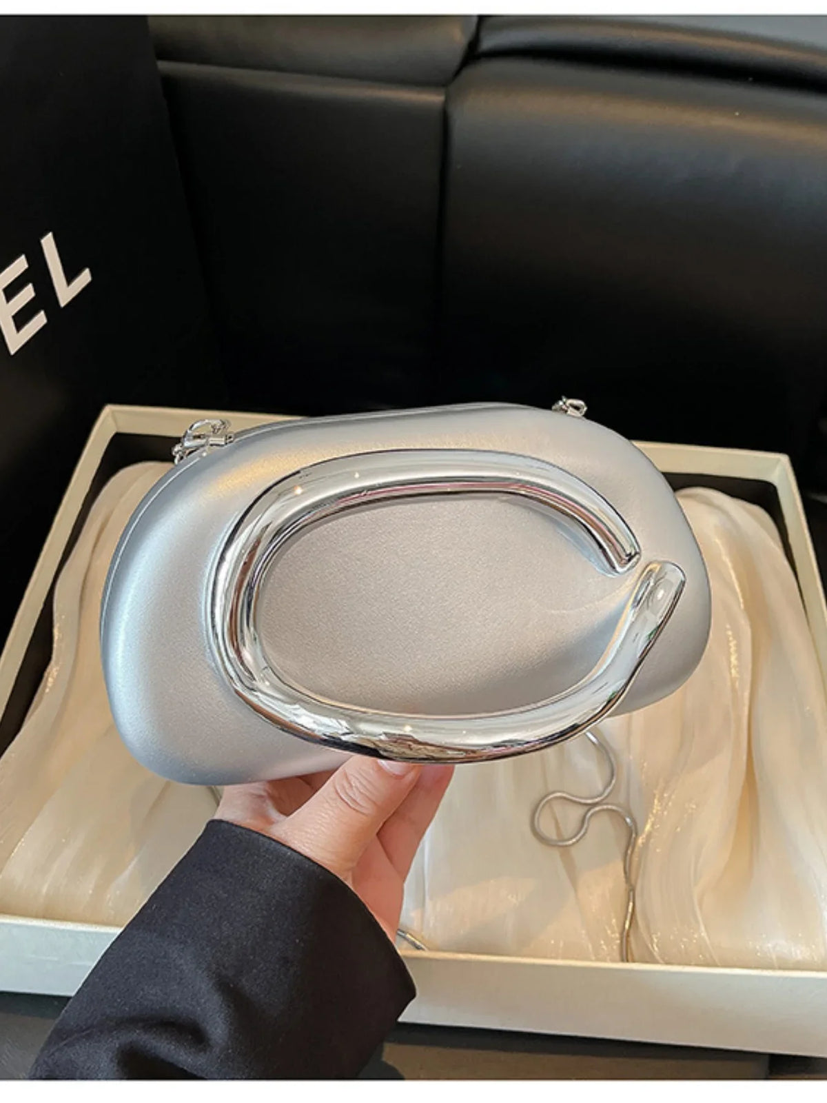 Shell-shaped silver handbag with a glossy handle, displayed in a gift box with silk-like lining.