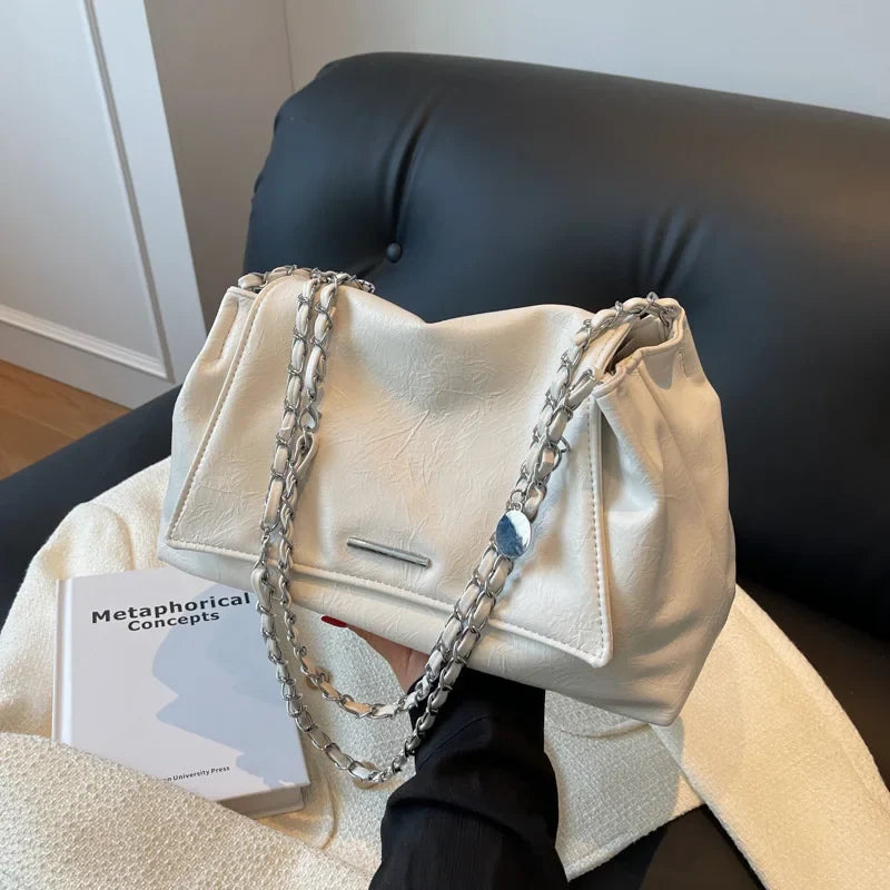Soft white leather shoulder bag with silver chain straps and a flap pocket, resting on a black couch.