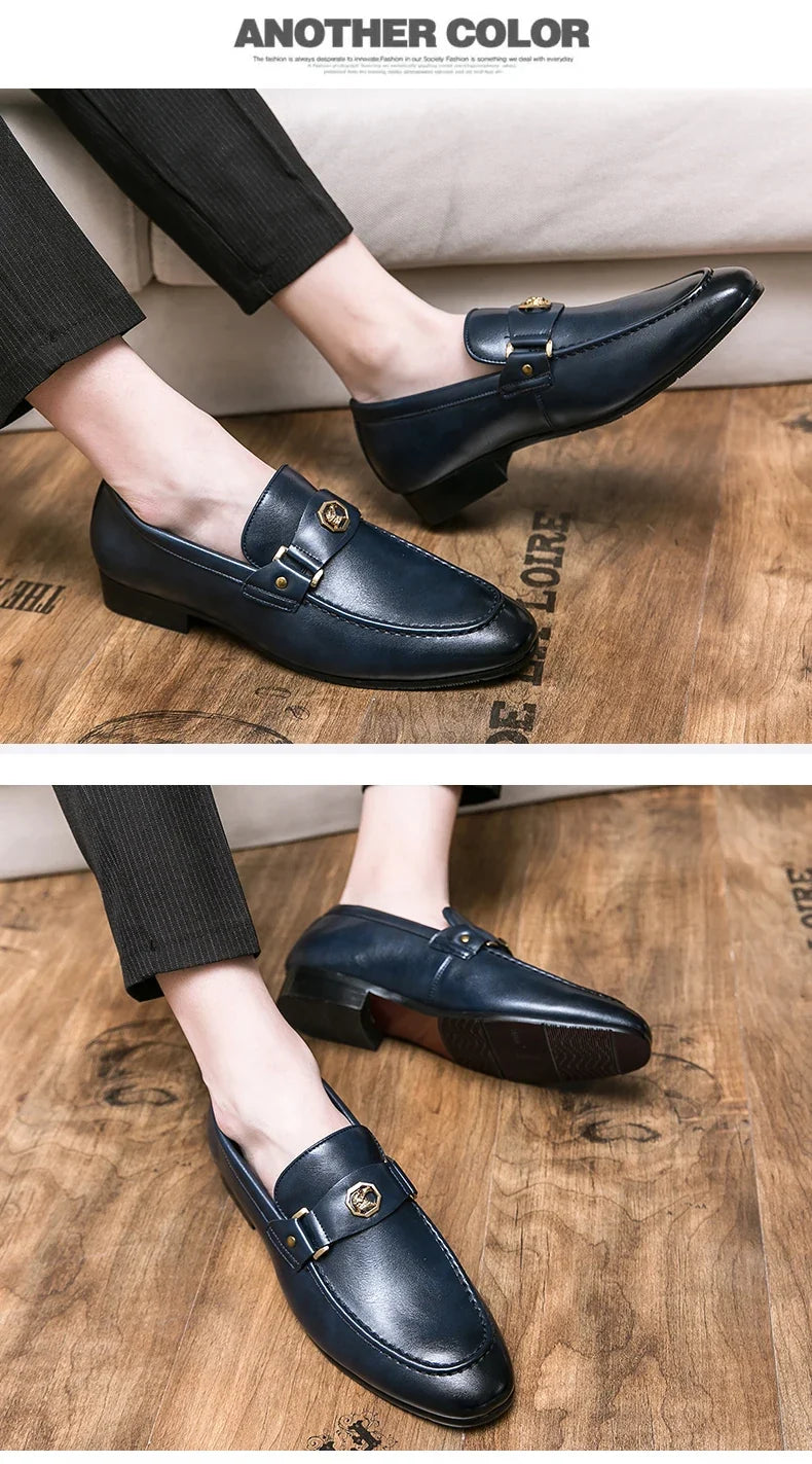 Navy blue slip-on loafers with a round toe and gold metal buckle, presented with tailored black pants on a wooden floor.
