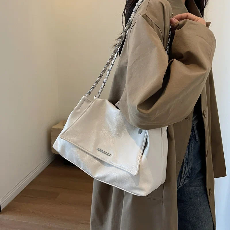 White soft leather handbag with a flap pocket, worn casually on a shoulder with a chain strap.