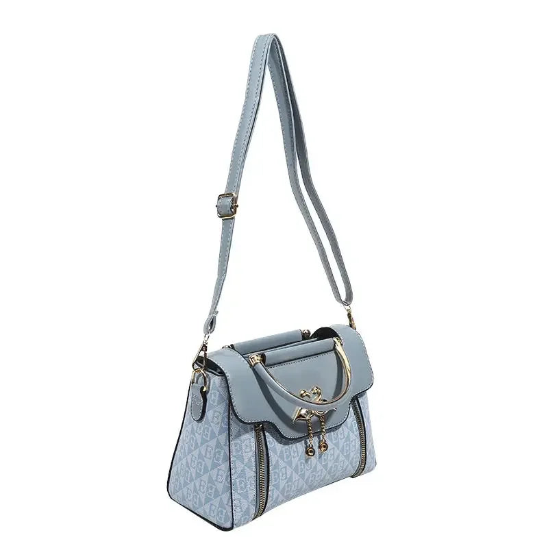 Light blue handbag in a rectangular shape, featuring an embossed pattern and gold-tone details; worn as a shoulder bag.