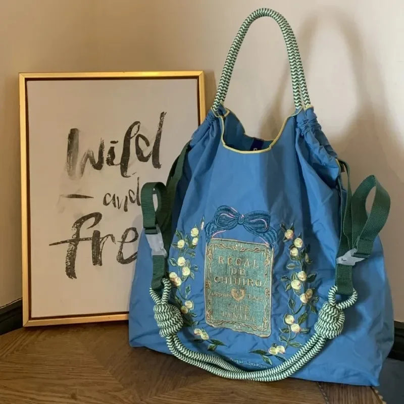 Large blue nylon tote bag with embroidered floral design, dual green handles, and casual style for easy carry.