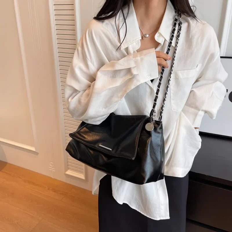 Black soft leather shoulder bag with a chain strap, worn underarm, paired with a white oversized shirt.