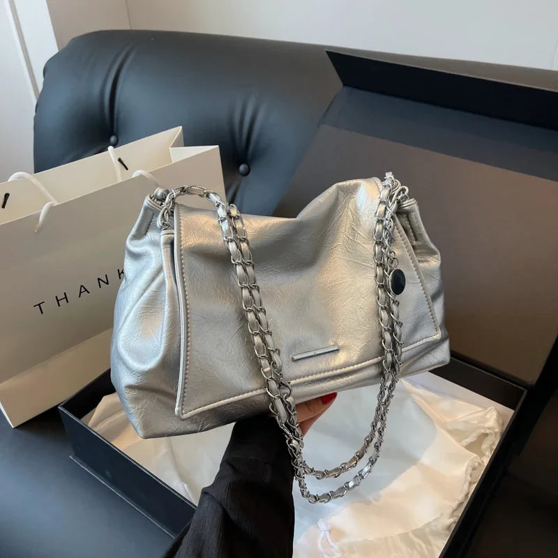 Silver shoulder bag with a soft leather finish, featuring a chain strap and a large capacity, held by a model.