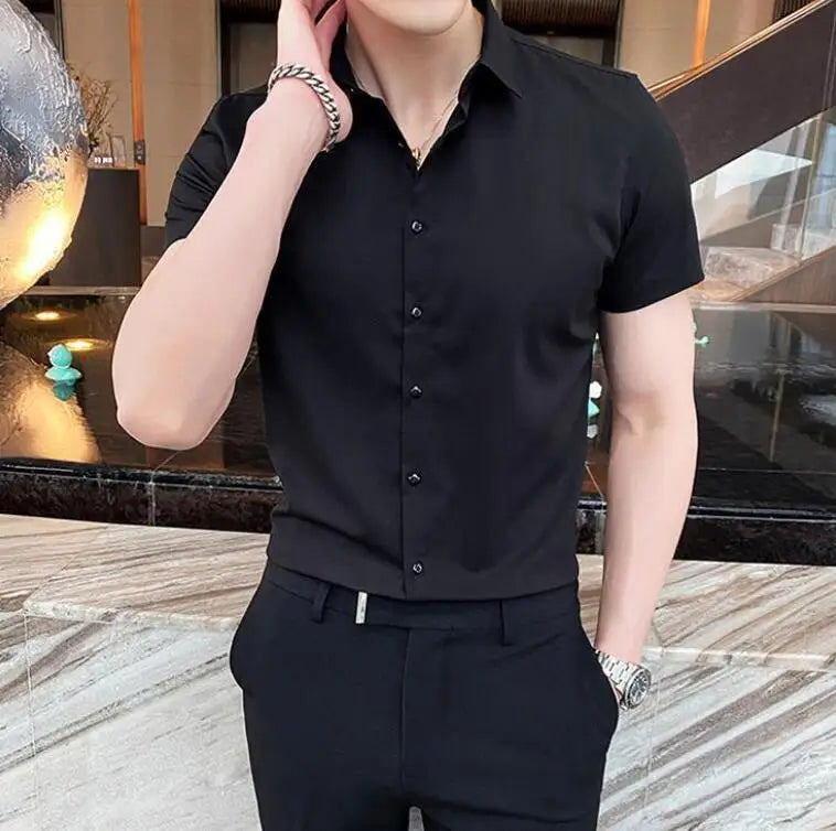 Short-sleeve black shirt with a square collar, worn by a model, paired with dark pants, showcasing a sleek, formal style.
