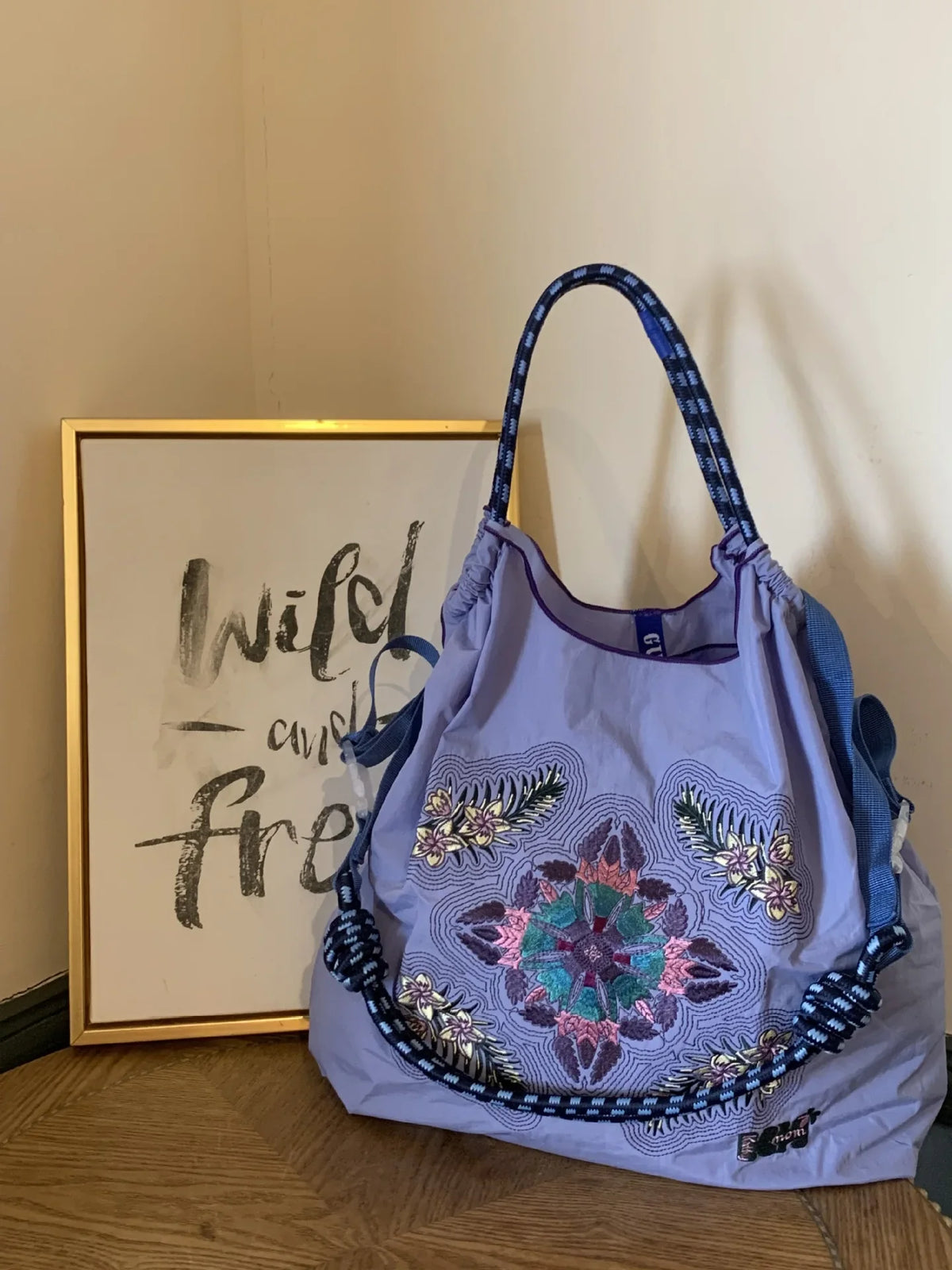 Large lavender nylon tote bag featuring colorful floral embroidery and a braided strap, styled for casual use.