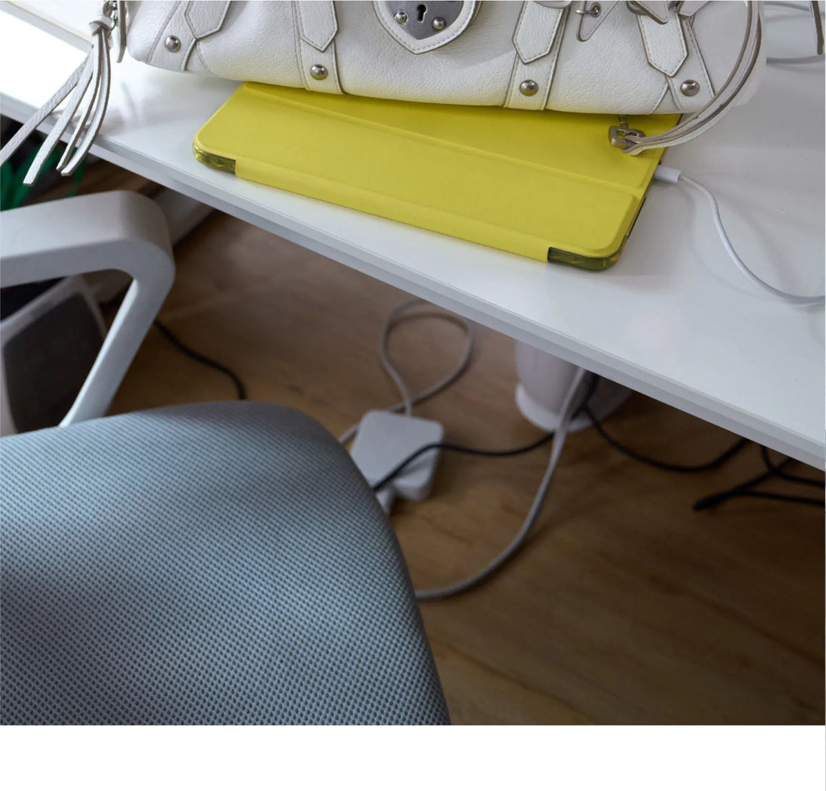 White handbag with silver hardware and tassels, resting on a bright yellow tablet cover atop a desk.