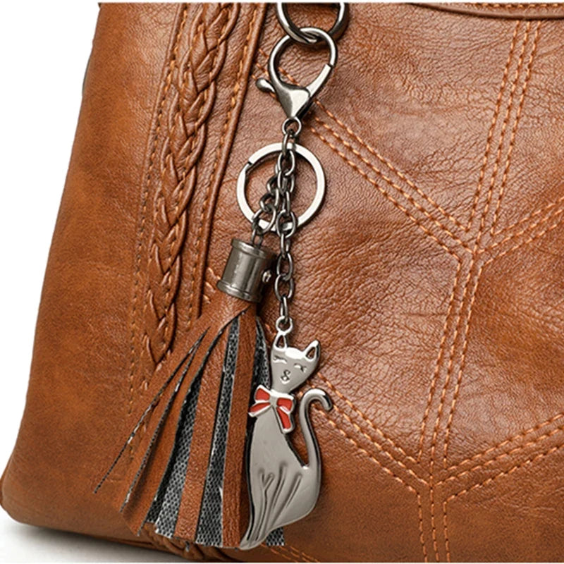 Tan leather tote handbag featuring a braided strap and a cute cat charm with a bow, showcasing a quilted design.