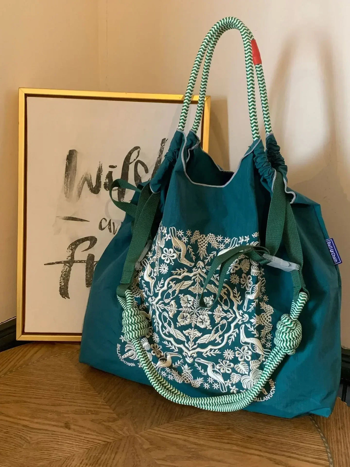 Teal nylon tote bag with intricate white embroidery, featuring rope handles and a casual design, ideal for daily use.