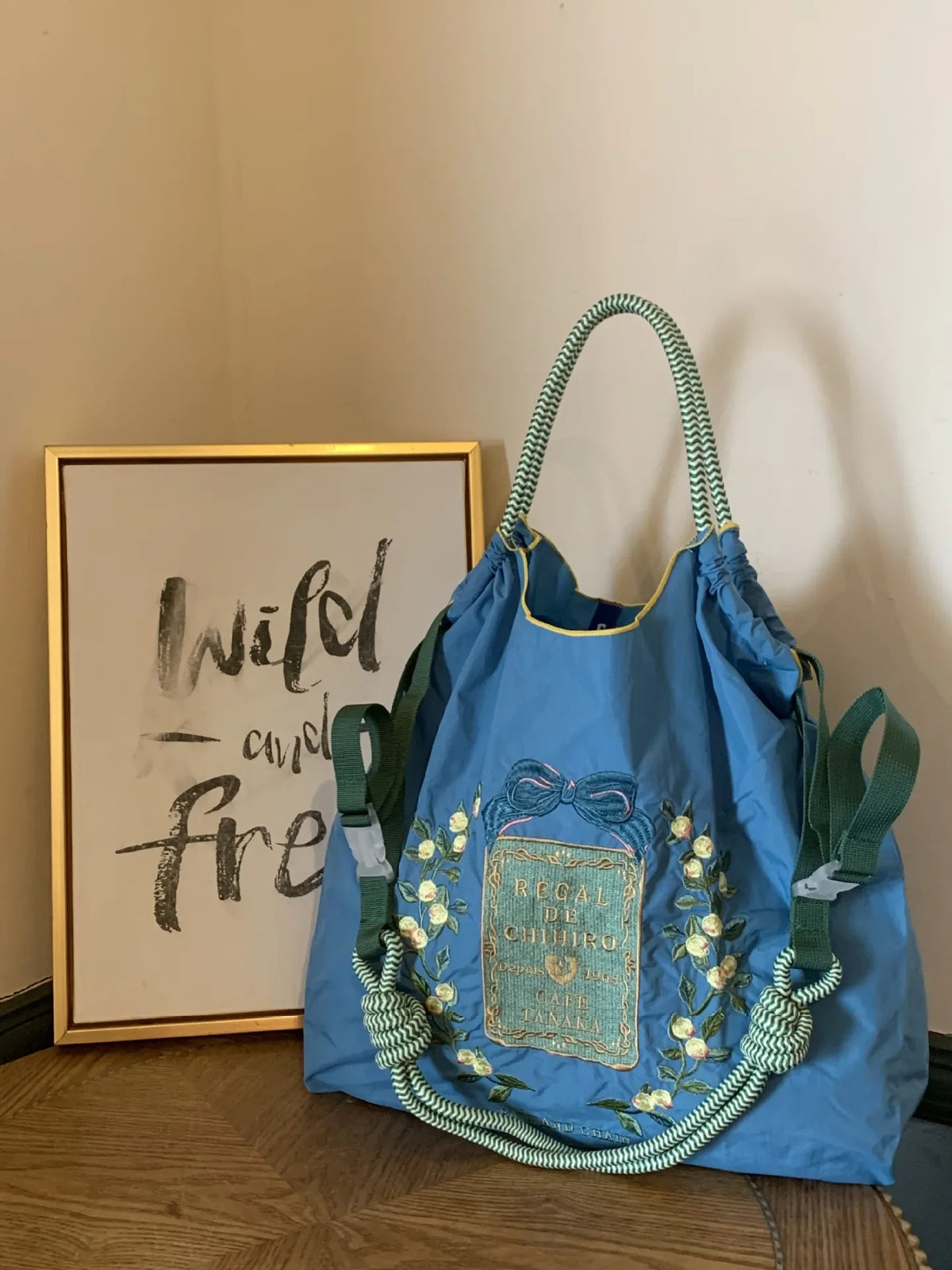 Light blue nylon tote bag with green handles and embroidered floral details, featuring a large capacity and casual style.