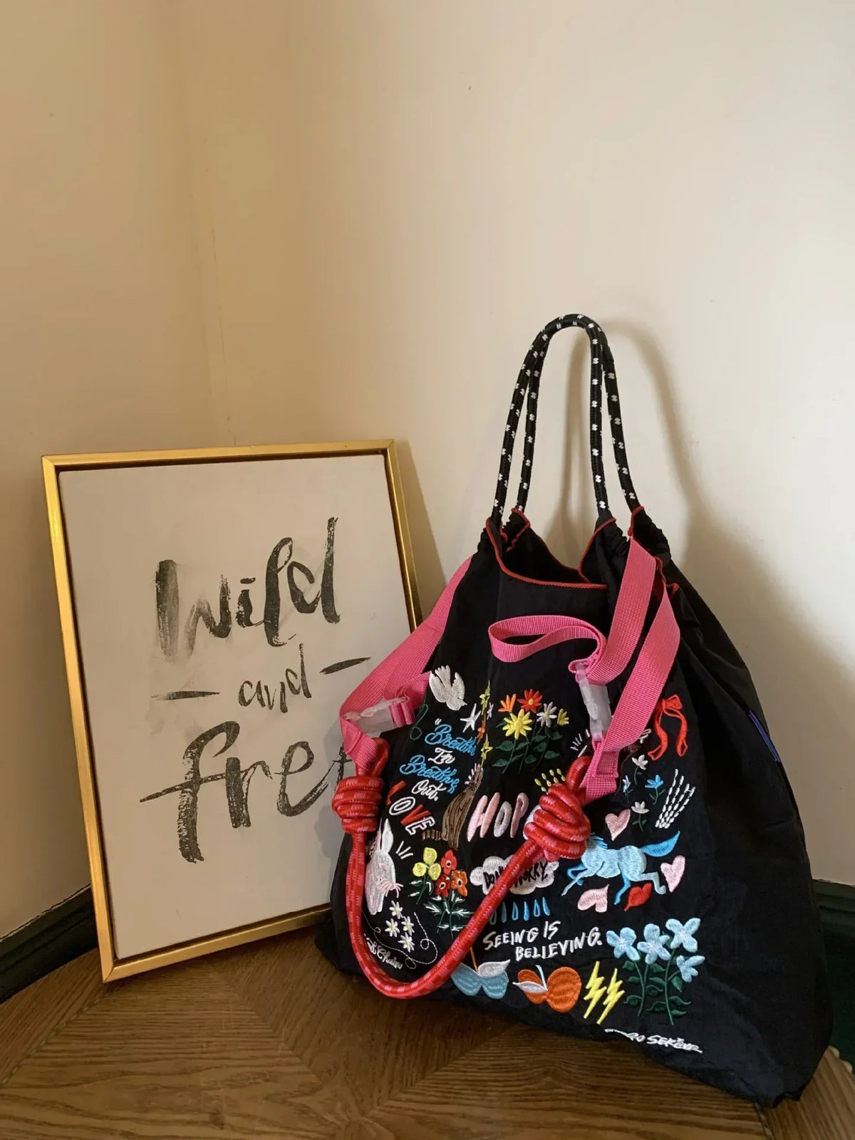 Large black nylon tote bag with colorful embroidery and pink handles, styled as a casual single-shoulder bag.