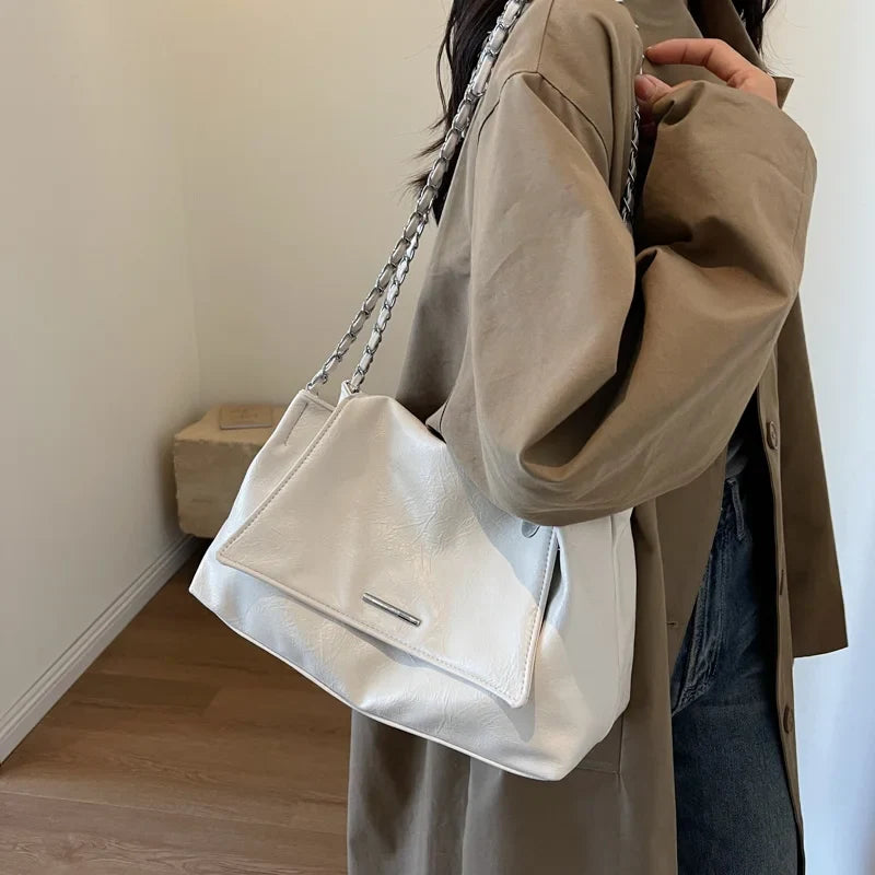 Silver chain-strap handbag in soft white leather, worn casually underarm, featuring a flap pocket and spacious interior.