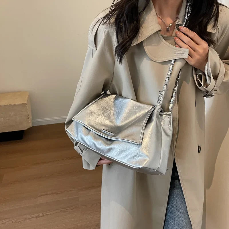 Silver shoulder bag with a soft leather finish, styled casually under the arm, paired with a beige coat.