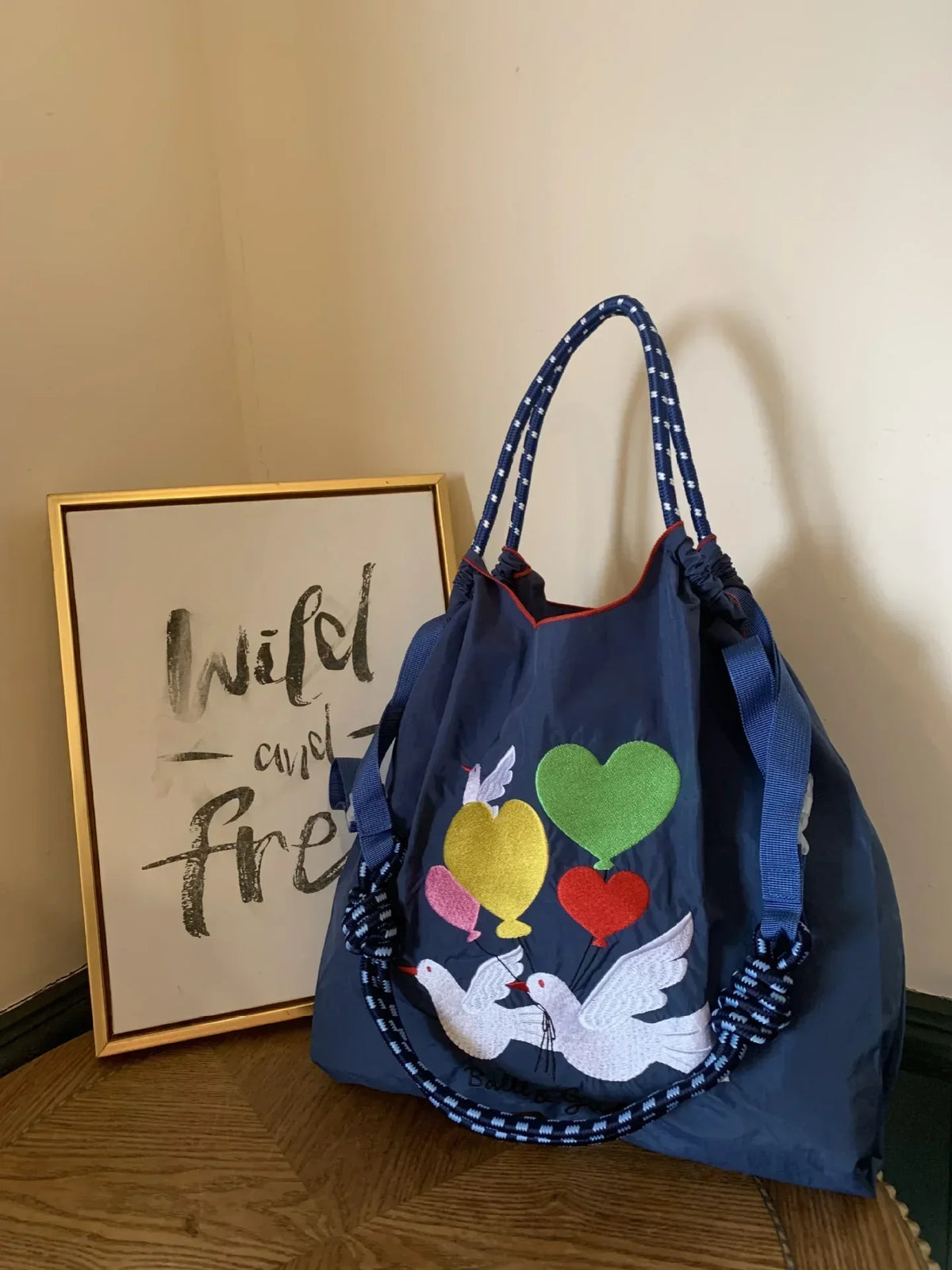 Large navy tote bag with embroidered birds and heart balloons, featuring blue and white patterned handles.